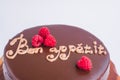 Round chocolate cake with raspberry decor and the inscription - Bon appetit. On a wooden stand isolated on a white background. Royalty Free Stock Photo