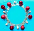 Round Christmas silver tinsel frame red baubles on bright blue background. Royalty Free Stock Photo