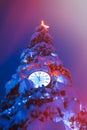 Round clock with illumination on the Christmas tree. Hands on the clock show without five twelve. Selective focus