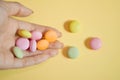 Round colored candies lie in a bunch on hand on yellow color, with copyspace, closeup Royalty Free Stock Photo