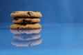 A round cookie with chocolate drops is stacked on top of each other on a blue bright saturated background with a reflection side v