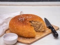 Round-cut homemade bread, baked from coarse flour lies on a wooden kitchen board. Next to the salt shaker with coarse