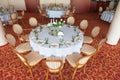Round dining tables, covered with white cloth, served with green glasses and ornate with flowers, stand on a colored carpet Royalty Free Stock Photo