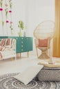 Ethno carpet on white floor of stylish bedroom interior with green furniture and wicker peacock chair