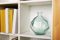 Round faceted green glass vase on a square white bookshelf