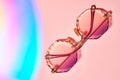 Round, female, with colored lenses and grained edges, sunglasses on pink background.