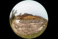 Round fisheye photo of a dirt country road on a cloudy autumn day. 180 degree wide angle view