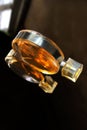 Round flat bottle of orange perfume on a dark background on a glass