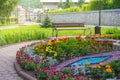 Round flower bed with colorful decorative flowers and plants, garden bench stands on the paving tiles, a beautiful recreation area Royalty Free Stock Photo