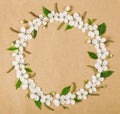 Round frame wreath made of white spring flowers and green leaves on brown paper background. Flat lay. Royalty Free Stock Photo