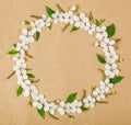 Round frame wreath made of white spring flowers and green leaves on brown paper background. Flat lay. Royalty Free Stock Photo