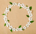 Round frame wreath made of white spring flowers and green leaves on brown paper background. Flat lay. Royalty Free Stock Photo