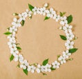 Round frame wreath made of white spring flowers and green leaves on brown paper background. Flat lay. Royalty Free Stock Photo