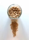 A round glass jar with chickpeas inside and in front of a set of more chickpeas on a white table