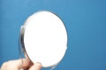 Round hand mirror with isolated reflection on textured blue wall background