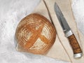 Round handmade bread, top view. It is located on a gray background, next to a cotton napkin and a knife