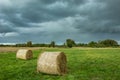 Round hay bales lying on a green meadow and dark rainy clouds in the sky Royalty Free Stock Photo