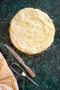 Round layered napoleon cake with custard and sprinkled crumbs, knife, towel and mixer on a green marble table, top view. The