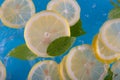 Round lemon slices falling deeply under water with green mint leaves on blue background. Selective focus Royalty Free Stock Photo