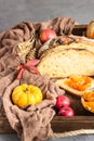 Round loaf of artisan wheat bread with pumpkin and apple in a wooden tray.