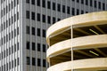 Round, metal clad parking garage in faded yellow backed by monochrome skyscraper