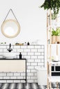 Round mirror above white washbasin in modern bathroom interior with plants. Real photo