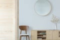 Round mirror above wooden chair and cabinet in minimal anteroom interior with decor