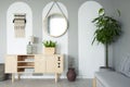 Round mirror hanging on the wall in real photo of grey living room interior with retro cupboard with lamp and books and fresh