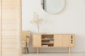 Round mirror on white wall above wooden cabinet in simple anteroom interior with armchair