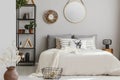 Mirror and wooden clock on the wall of elegant bedroom with beige bedding and white warm blanket, real photo