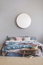 Round mirror in wooden frame on grey wall of elegant bedroom interior with comfortable bed with pastel, blue and pink bedding Royalty Free Stock Photo