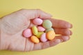 Round multicolored candies lie in a bunch on woman hand on yellow color, closeup Royalty Free Stock Photo