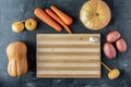 Round and oblong pumpkin, potatoes, turnips and carrots on a dark textured background around a bamboo cutting Board