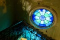 Round old stained glass window in a dark corridor with forged lattice stair and grungy dirty scratched walls. A