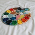 A round painter\'s palette rests on a white fabric surface. It features multiple vibrant Royalty Free Stock Photo