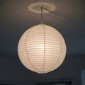 A round paper lantern with horizontal ribbing hangs from a ceiling. The lantern emits a Royalty Free Stock Photo