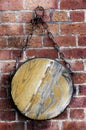 Round piece of blank wood hanging on a chain on red bricks wall. Royalty Free Stock Photo