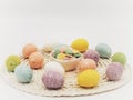 Round placemat topped with Easter eggs covered in sparkly string and a white bowl of pastel colored white chocolate mint candies