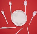 Round plate and stack of plastic forks and spoons on red background Royalty Free Stock Photo