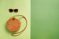 Round rattan bag, sunglasses on green background. Banner. Top view with copy space. Trendy bamboo bag and white shoes