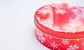 Round, red cookie and baked goods aluminum tin container decorated with white snowflake print pattern, resting on natural snow. Royalty Free Stock Photo