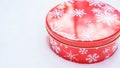 Round, red cookie and baked goods aluminum tin container decorated with white snowflake print pattern, resting on natural snow. Royalty Free Stock Photo