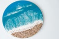 Round resin art painting with blue ocean waves and beach on white background. Epoxy art