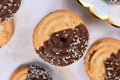 Round ring shaped spritz biscuits with half side glazed with chocolate and topped with coconut sprinkles
