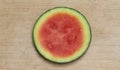 Round slice of pink seedless watermelon with a yellow and green rind, centered on a worn, pale brown cutting board Royalty Free Stock Photo