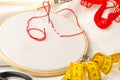 Round stitching or embroidery frame with red stitching and sewing tools