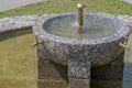 Round stone fountain made of granite and marble with cross shaped pedestal with central rounded metal golden nozzle and four taps Royalty Free Stock Photo