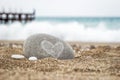 A round stone with a heart symbol lies on the golden sand of the beach on a blurred background of the sea Royalty Free Stock Photo