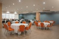 Round table with a white tablecloth, orange and black chairs in a modern restaurant or banquet room of a luxury hotel. Catering