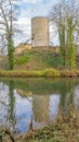 Round tower of castle ruins on a hill, bare trees, moat with the tower reflected in the water surface